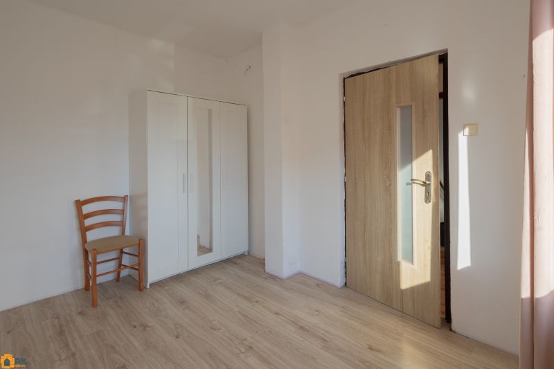 A room in a family house with a wooden decor floor, a wardrobe, and a chair.