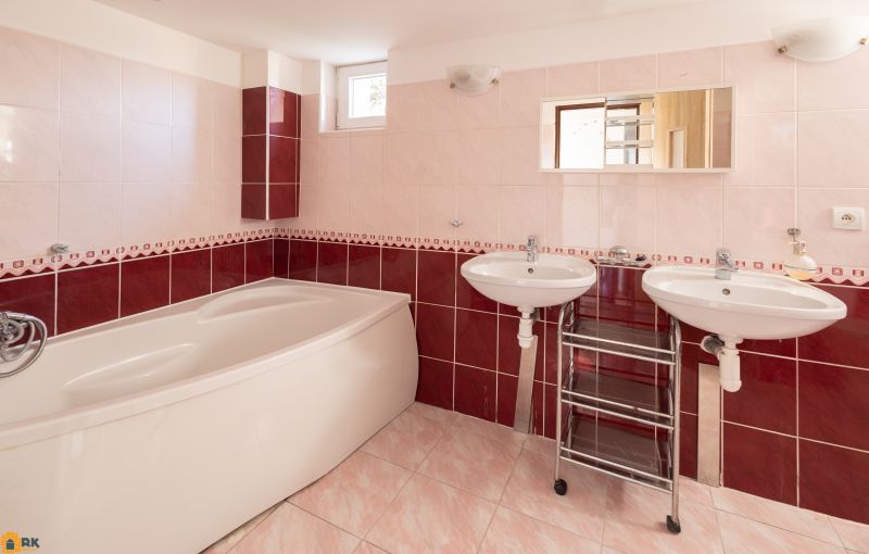 A bathroom in a family house with a corner bathtub and two sinks on pink-red tiles.
