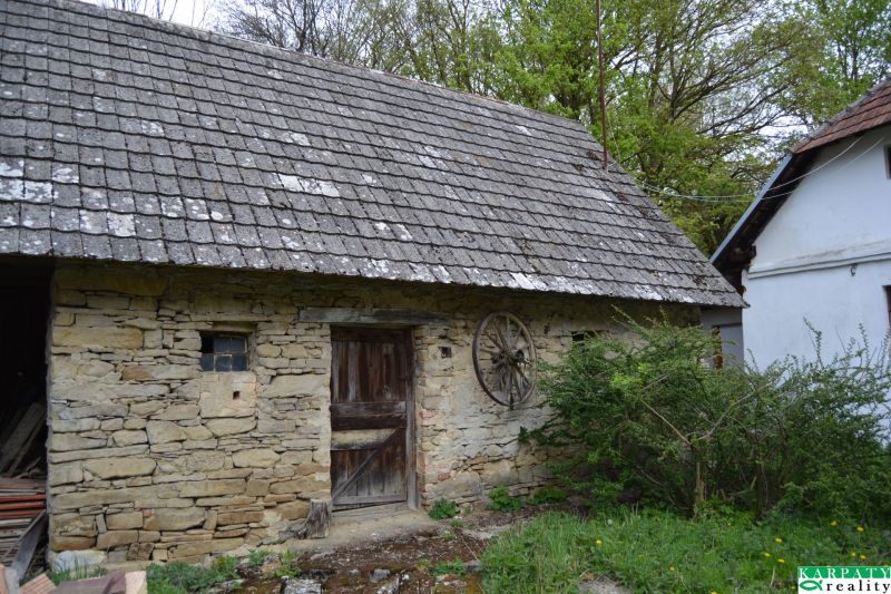 A stone barn next to a family house in Bukovec with wooden doors and a tiled roof.