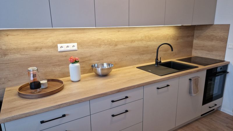 A kitchen in a 3-room apartment with a wooden decor floor, light cabinets, and a black sink.