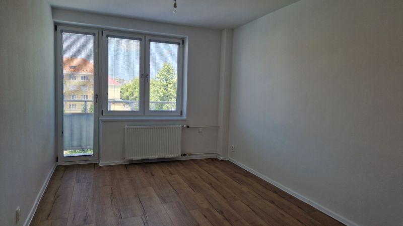 A room in a 3-room apartment with a wooden decor floor, a large window, and a radiator.