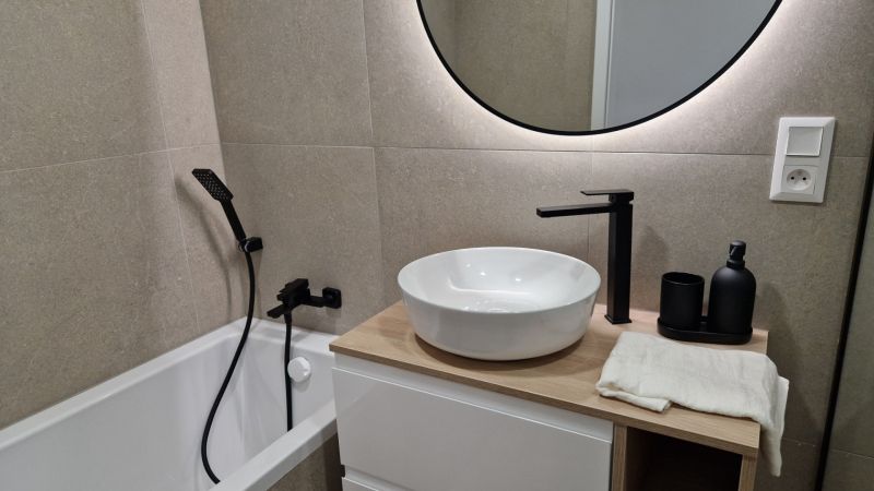 A bathroom in a 3-room apartment with a round mirror and modern faucets.