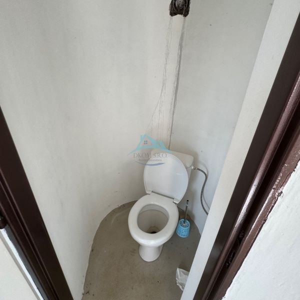 Simple toilet in a cabin with a wall without tiles and a plastic toilet.