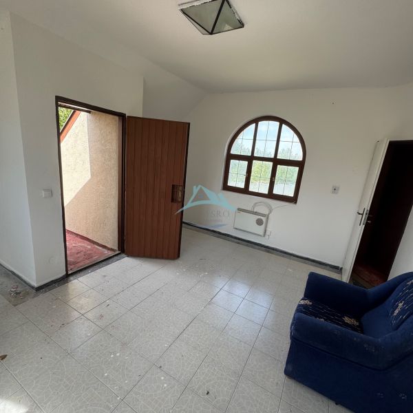 A room in a cottage with doors to the terrace, a tiled floor, and a dark blue armchair.