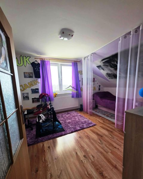 Children's room with purple curtains, carpet, bed, wooden decor flooring.