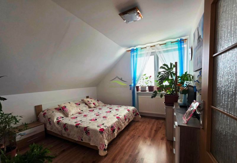 Bedroom in a family house with a bed, wooden decor flooring, and houseplants.