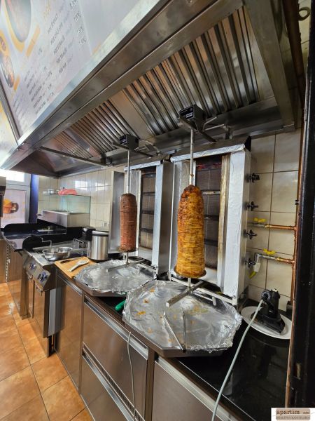 A kitchen in a gastro space with equipment for preparing kebab, including a range hood.