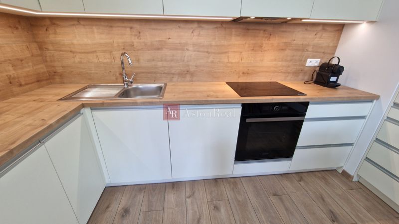 A kitchen with a wooden decor countertop and built-in appliances in a 2-room apartment.