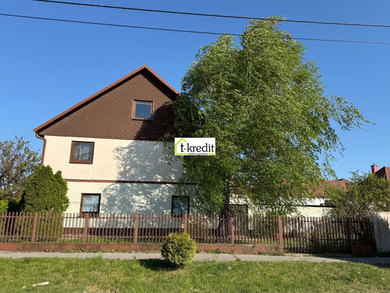 A family house in Zlaté Moravce, a garden with trees, a fence, and a blue sky.