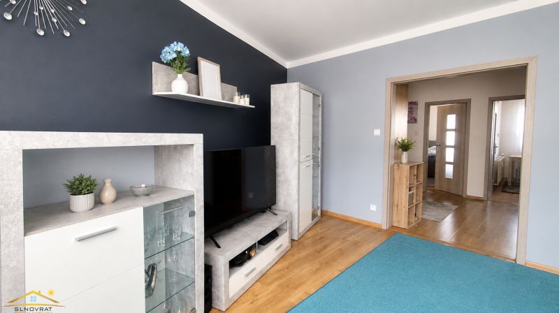 Living room in a 3-room apartment with shelves, a television, and a wooden decor floor.
