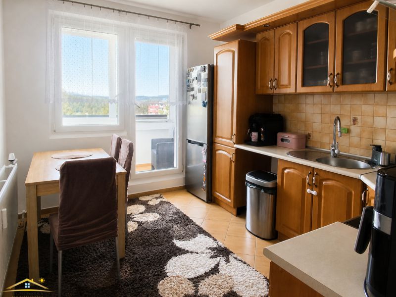 A kitchen in a 3-room apartment with wooden cabinets, a dining table, and a large window.