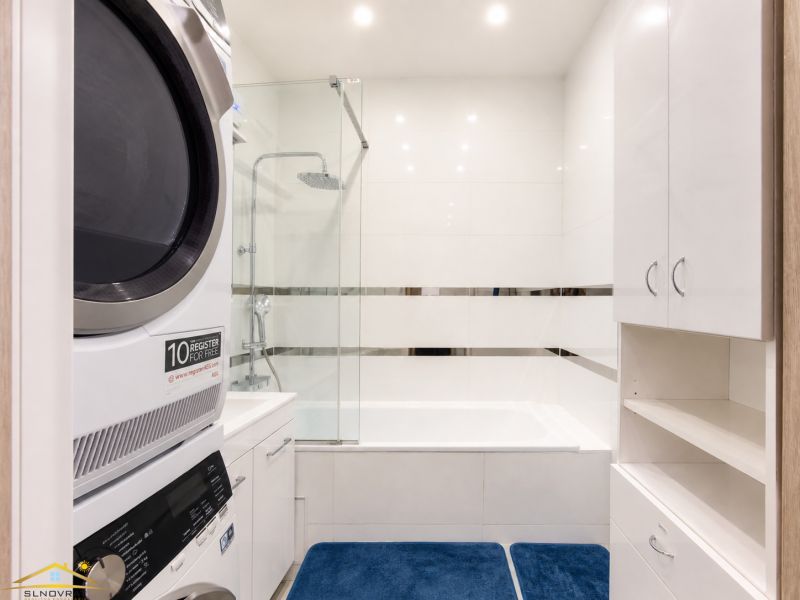 A bathroom in a 3-room apartment with a bathtub, a washing machine, and white furniture.