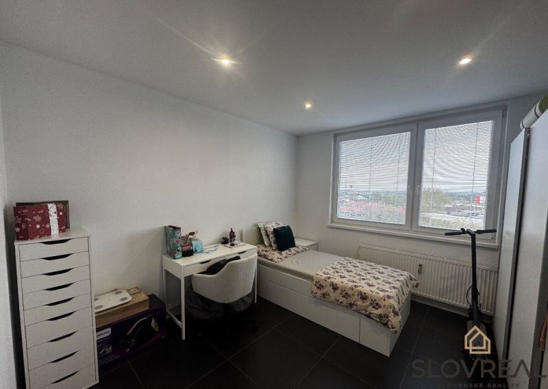 A room in a 3-room apartment with a bed, a table, and large windows.