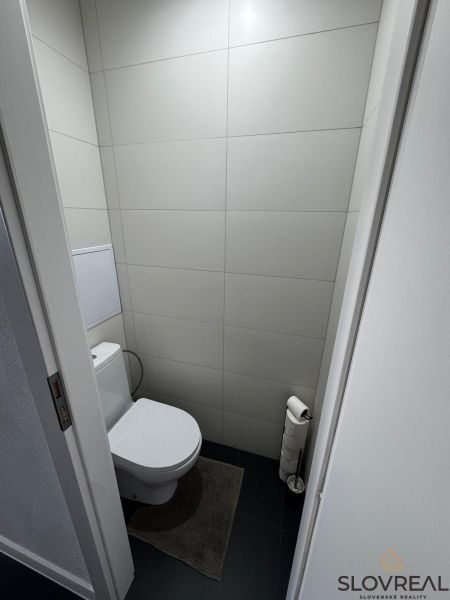 A toilet in a 3-room apartment with minimalist gray tiles and a dark floor.