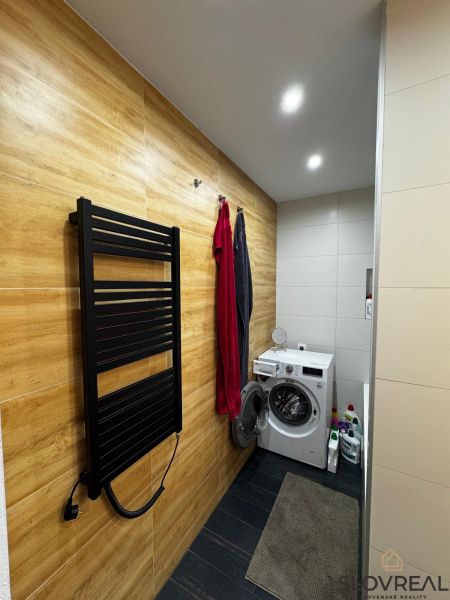 Bathroom with a washing machine, floor with wooden decor, towel dryer in a 3-room apartment.