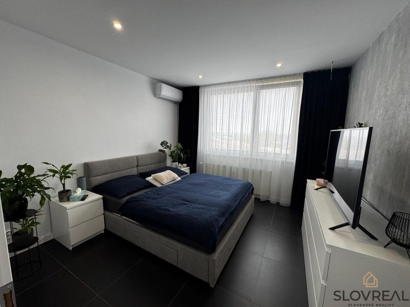 A bedroom in a 3-room apartment with a large bed, a television, and houseplants.