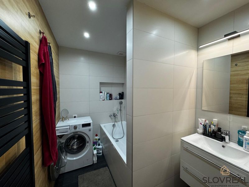 Bathroom in a 3-room apartment with a bathtub, washing machine, and wooden wall decor.