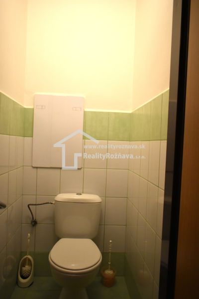 A bathroom with green and white tiles and a toilet in a 3-room apartment.