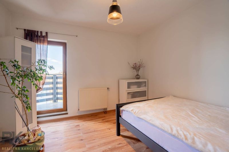 A bright bedroom in a 4-room apartment with wood-patterned flooring, a plant, and a balcony.
