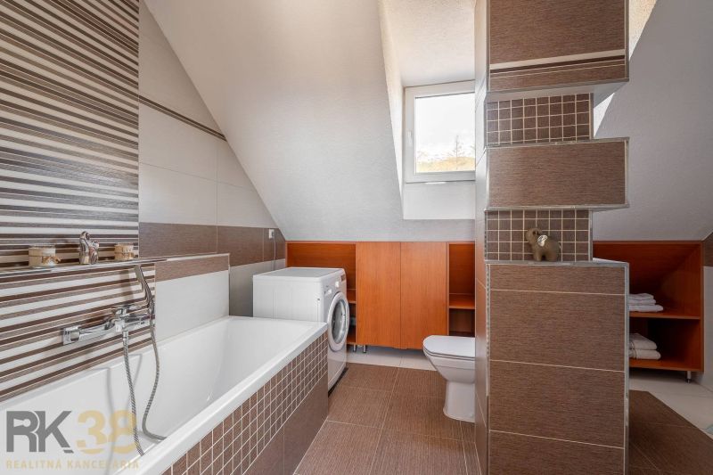 A bathroom with a pitched roof, a bathtub, a washing machine, and brown tiles in a 4-room apartment.