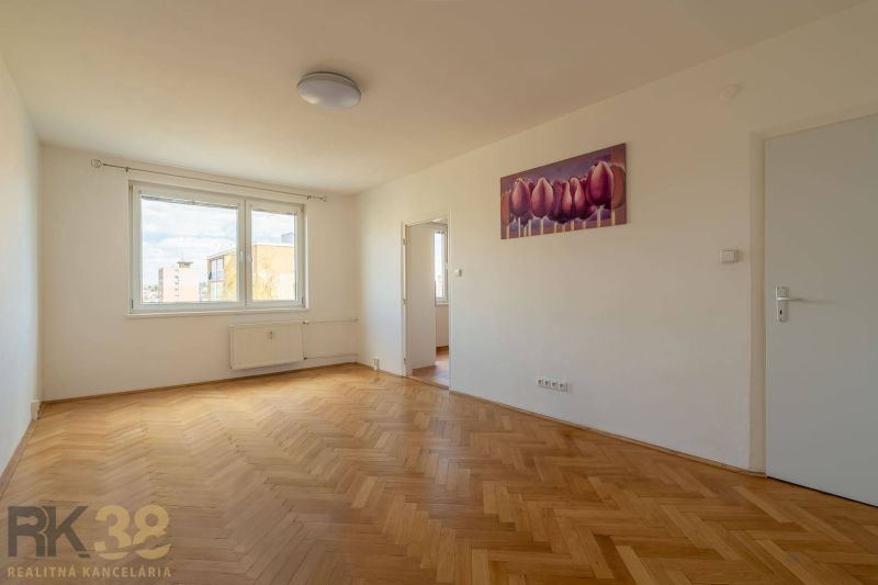 A spacious room with a large window, wooden decor flooring, and a painting in a 4-room apartment.