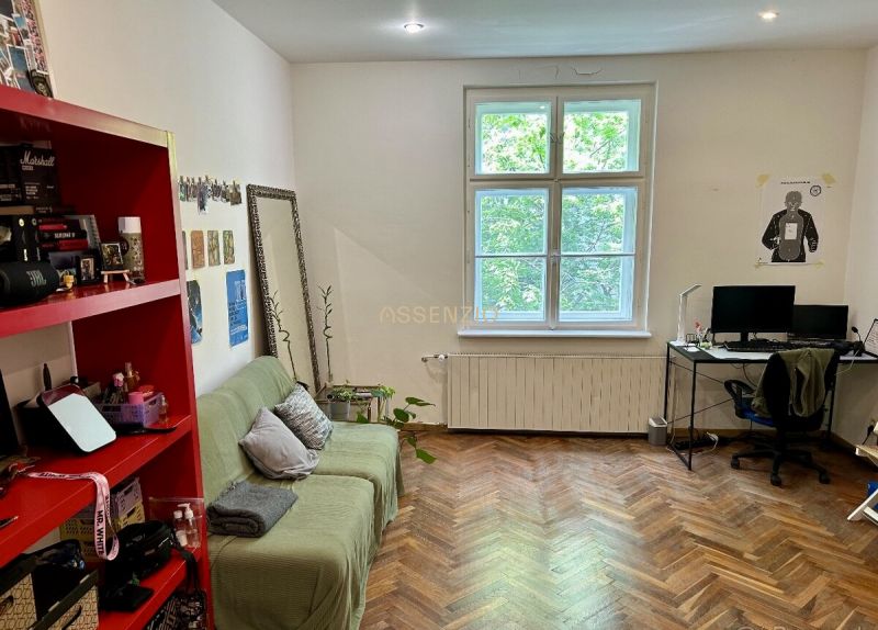 Living room in a two-room apartment with a wood-patterned floor, a sofa, and a computer desk.