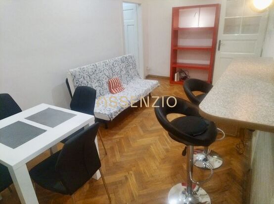Living room of a two-room apartment with a wooden decor floor, a dining table, and bar stools.