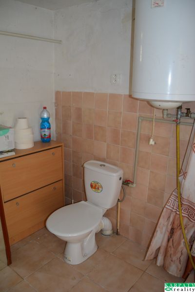 Bathroom in a family house with a toilet, furniture, a bottle, and a water heater.