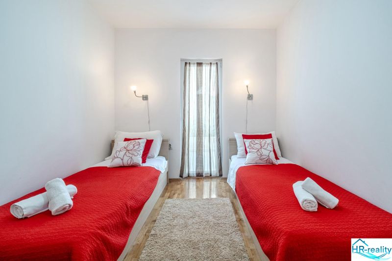 A recreational apartment with two beds, a red blanket, and a wooden-patterned floor.