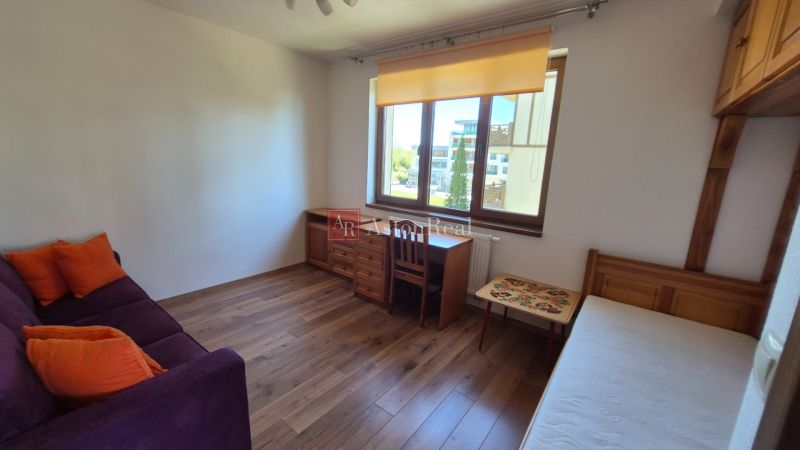 A room in a recreational apartment with a sofa, bed, desk, and wooden decor flooring.