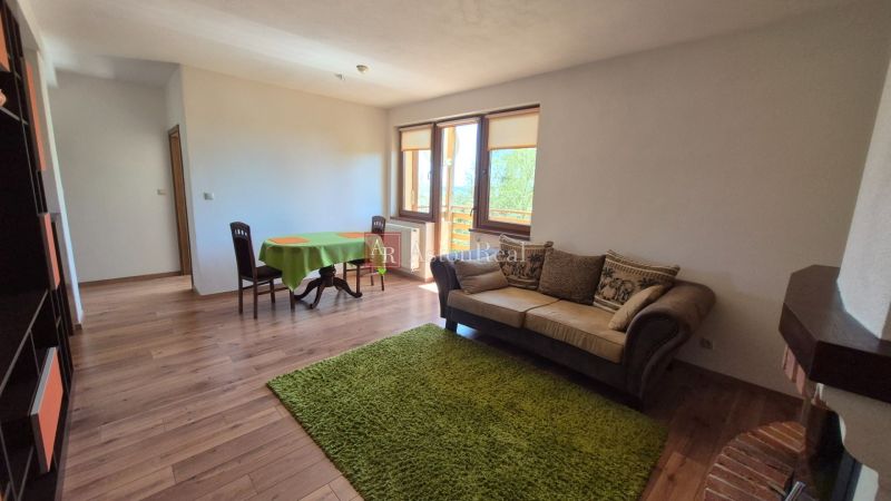 Living room with a sofa, dining table, shelf, and wooden decor flooring in a holiday apartment.
