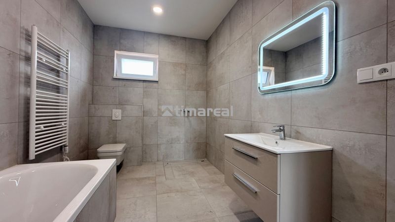 A bathroom in a family house with a bathtub, shower, ladder radiator, and backlit mirror.