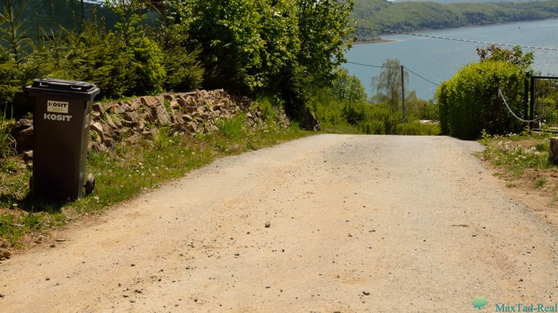 Paved road, trash can, and view of the lake in Nova Kelc, Recreational grounds.