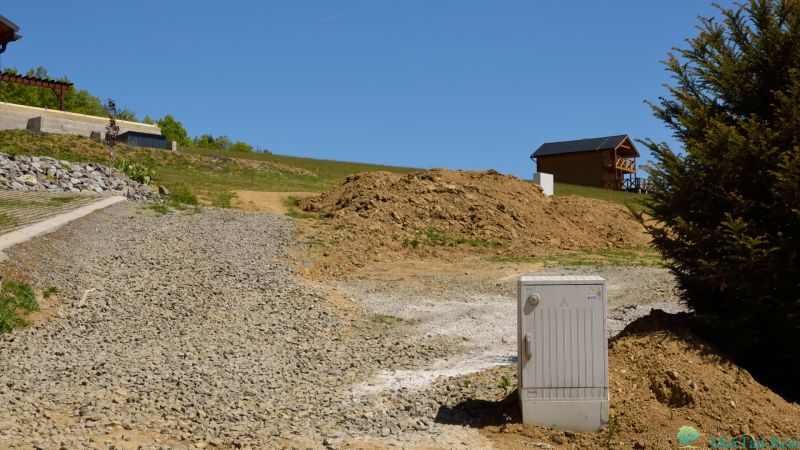 Recreational plots in Nová Kelča, gravel road, wooden house, slopes and vegetation.