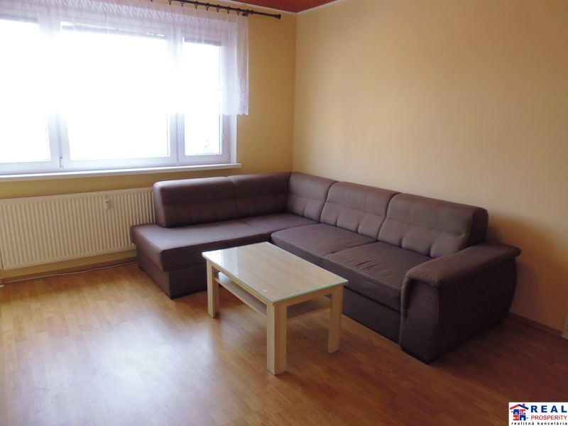 A bright living room in a two-room apartment with a sofa and a table on a wooden-decorated floor.