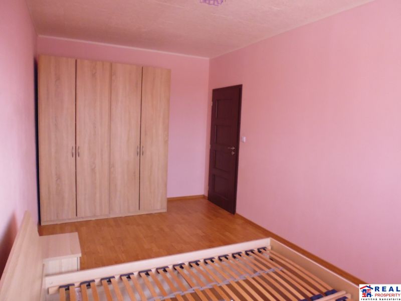 A room in a 2-room apartment with pink walls, a wardrobe, and a floor with a wooden decor.