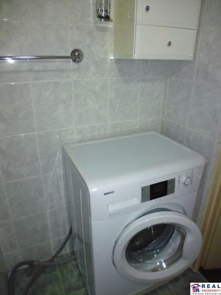 Bathroom in a 2-room apartment with a mirror, washing machine, and storage cabinets.