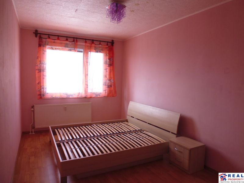 A bedroom with light pink walls, a bed, and a wood-patterned floor in a two-room apartment.