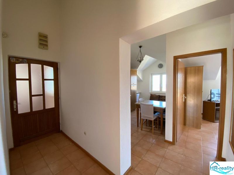 A hallway in a vacation apartment with a ceramic floor, a dining area, and a room in the background.