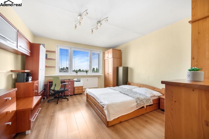 A bedroom in a three-room apartment with a bed, a desk, and a floor with a wooden decor.