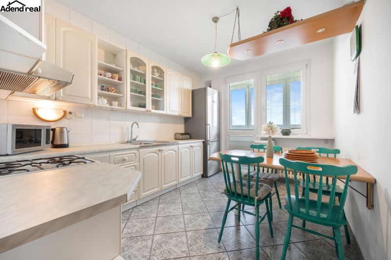 A kitchen in a 3-room apartment with a gas stove and a dining table with green chairs.