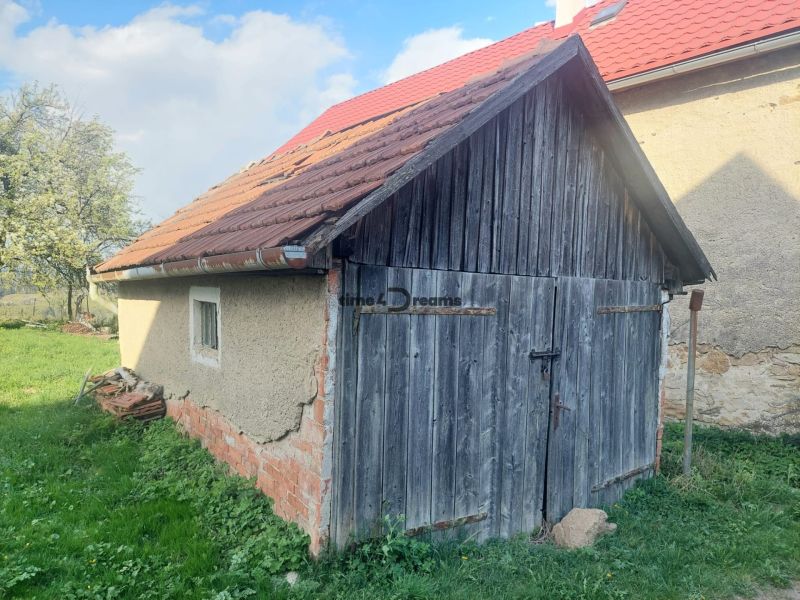 An old wooden garage on a residential plot in Budiná, surrounded by greenery and trees.
