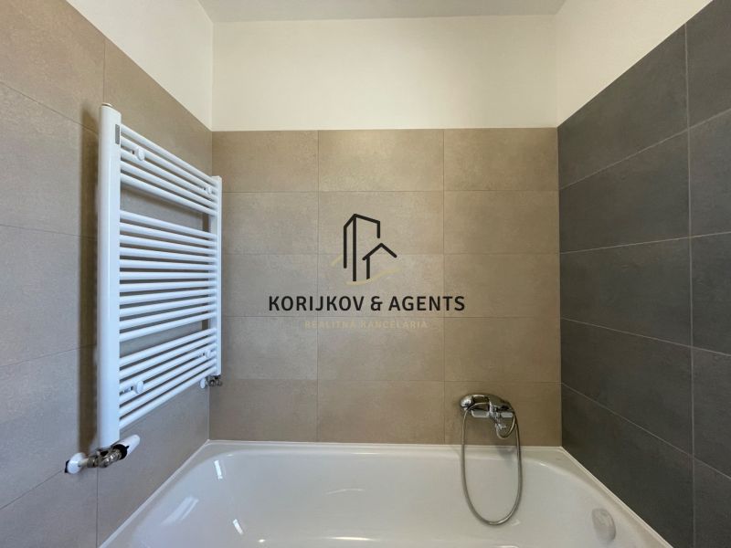 Bathroom in a 2-room apartment with a bathtub and combined beige-gray tiles.