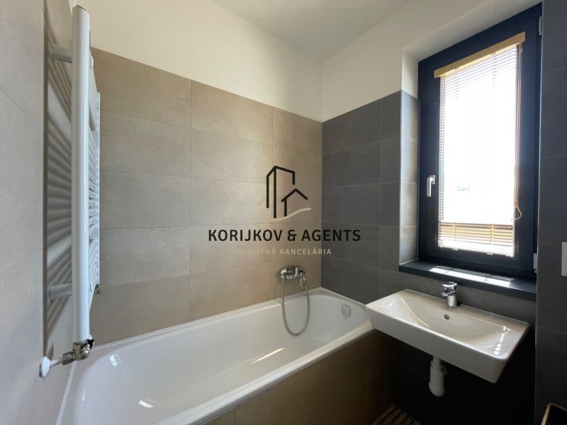 A bathroom in a 2-room apartment with a bathtub, sink, and window.