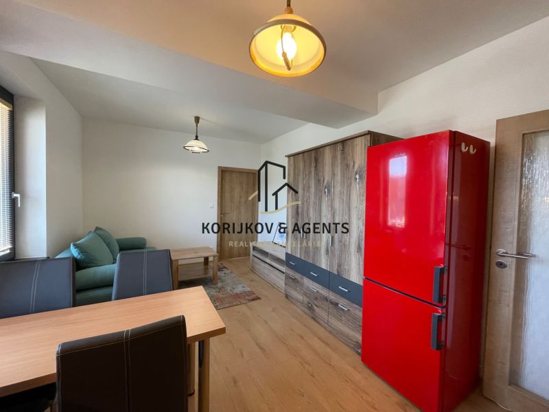 Living room in a two-room apartment with a wooden decor floor and a red refrigerator.