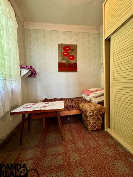 A room in a family house with a bed, a table, and a built-in wardrobe, a decorative carpet on the wall.