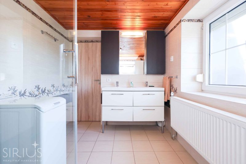 A bathroom in a family house with a wooden ceiling, a shower corner, and a white sink.