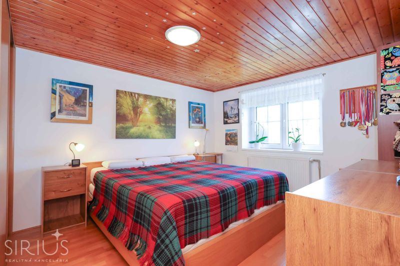 A bedroom in a family house with a wooden ceiling and a floor with a wood decor.