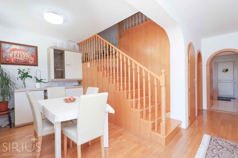 Dining room with staircase, wooden decor flooring, light chairs and table in a family house.