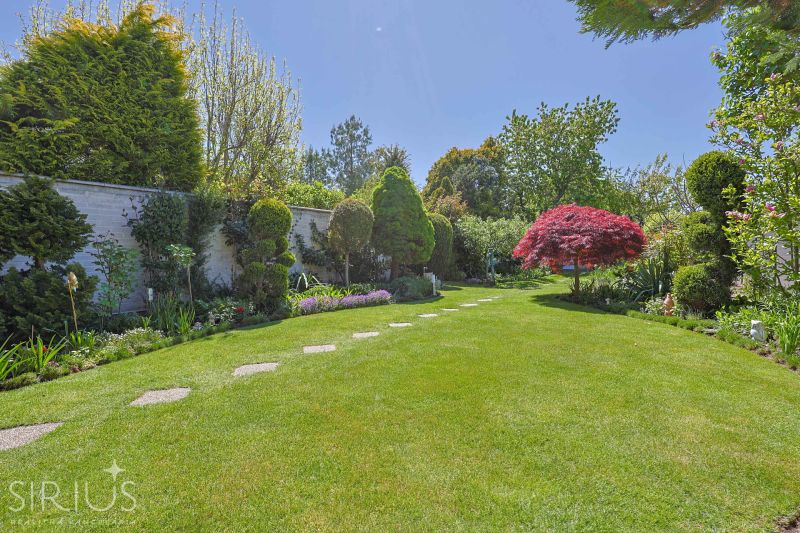 A garden with a manicured lawn and colorful trees by a family house.